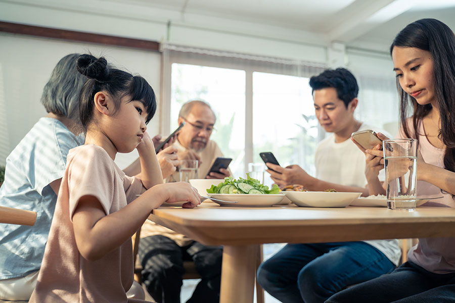 Child looks sad at dinner table, adults on cellphones